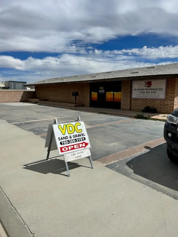 VDC Sand and Gravel storefront with open sign on parking lot under blue cloudy sky
